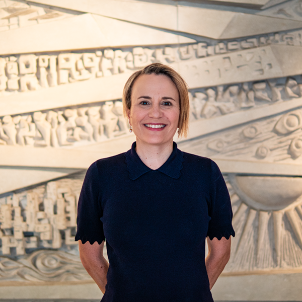 Head and shoulders portrait of Paula, wearing a black top, standing in front of a textured light-coloured background.