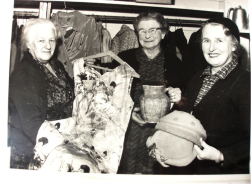Three women in the 1960s holding various items for sale for fundraising purposes.